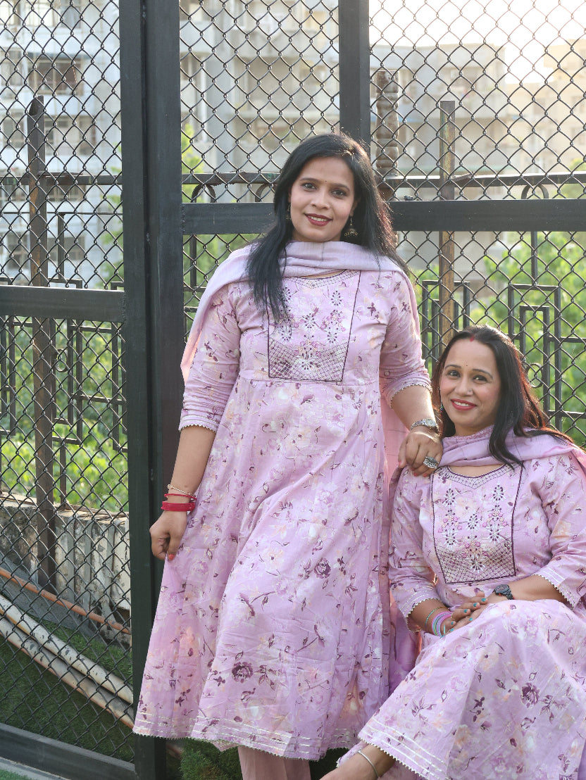 Two women in matching pink traditional outfits standing in front of a metal gate.