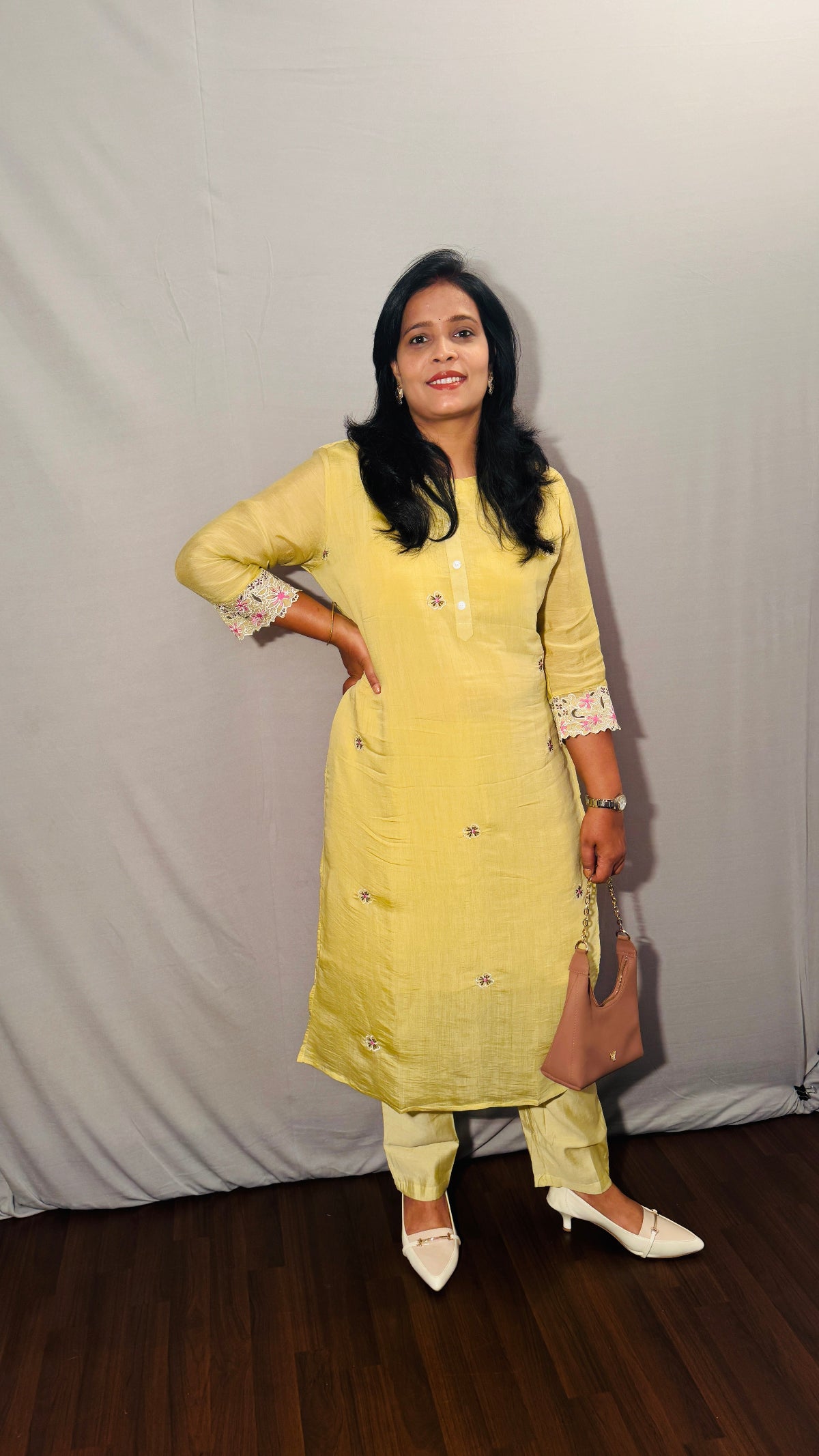 Woman in a yellow kurta with white shoes standing against a plain background